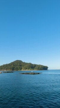 Serene summer scene: Slow-motion view from a moving boat reveals Tambo Island beyond mussel rafts on a sunny morning.