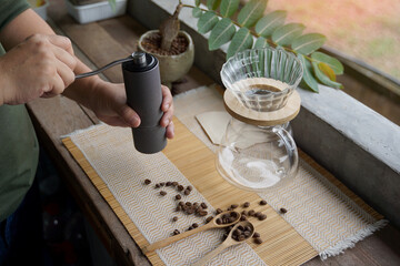 Asian man grinding coffee beans with grinder to easily drip black coffee at home, saving time and...