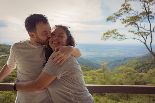 Happy couple in love, hugging at the top of a mountain and smiling to the camera with nice straight white teeth.