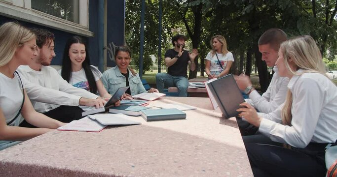 Diverse group of students having fun studying outside in the bench