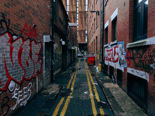 Alley way in Manchester England with bins rubbish / trash and random graffiti on the wall.