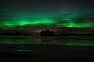Island in the middle of a frozen lake with the sky colored green by aurora boralis light in winter in Pirkanmaa, Finland