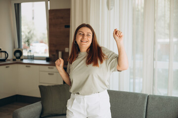 Fototapeta na wymiar Portrait of happy woman dancing, rejoicing and triumphing, feeling upbeat at home. Copy space. Young female enjoying carefree and leisure weekend