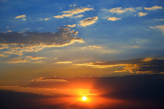 Dramatic sunset background with bright sun, blue sky and clouds. © Serghei V