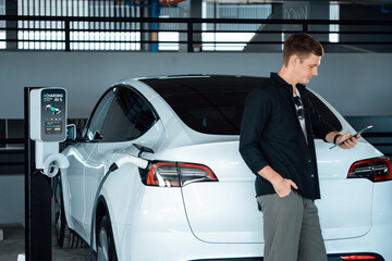 Young man travel with EV electric car to shopping center parking lot charging in downtown city...