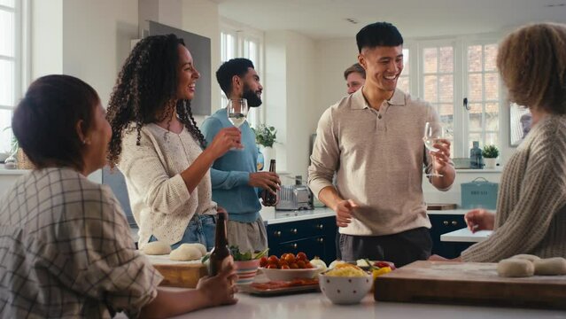 Multi-cultural group of young friends at home in kitchen with drinks making food for party - shot in slow motion