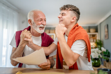 Senior man grandfather and caucasian man teenager boy grandson receive letter read good news student get scholarship or invitational letter from university share excitement real people