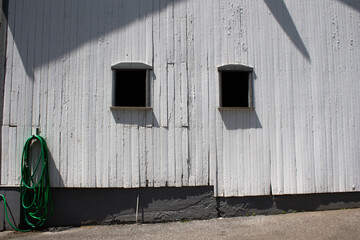 White farm wall, two windows and green water hose hooking on the wall