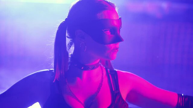 Sensual woman in leather BDSM mask moving seductively in swimming pool, neon