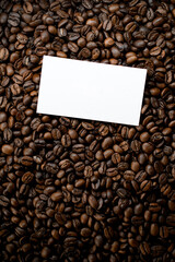 Freshly roasted coffee beans background with business card above, top view