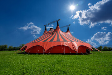 Red and black circus tent in green meadow with blue sky with clouds and sunshine © framarzo