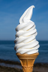 Soft whipped vanilla ice cream with chocolate stick in waffle cone in hands on blue sky background