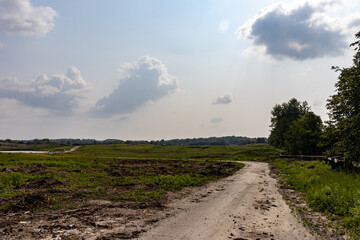 Dirt road - rural area - winding and bumpy - grass and shrubbery - blue sky with white clouds -...