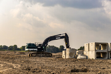 Construction site with large excavator digging and a partially constructed building in the background - blue sky with white clouds - barren ground with dirt and tire tracks. Taken in Toronto, Canada.