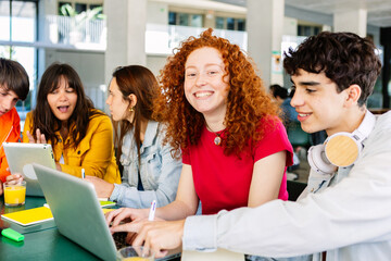 Happy young group of diverse students studying together and working together with laptop at cafeteria in campus college. Smiling joyful female looking at camera. Education concept.