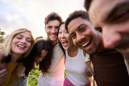 Crazy selfie of a group of young multirracial people embracing. Exited friends enjoying leisure and laughing a lot looking at camera outdoors. Diverse guys and girls community celebrating together
