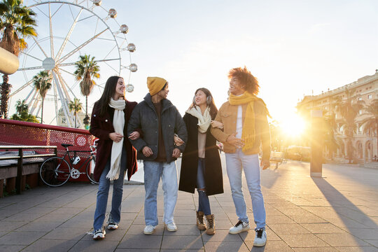Multiracial colleagues strolling through the amusement park holding on to each other winter day. Group of best friends meeting and hanging out together. People couple having fun and smiling outdoors. 