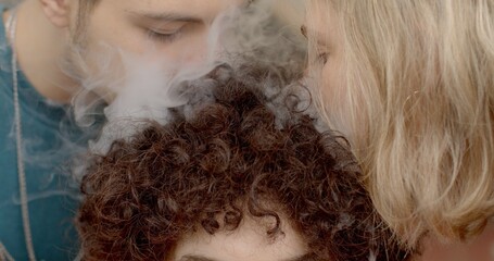 Closeup blowing smoke at person curly hair close up. Manipulating friendships. Students demonstrate arrogance in communication. Bullying in college university environment campus bullying. 