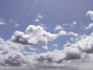 White clouds in the summer sun rays over blue sky background. Fluffy cumulus cloudscape shape