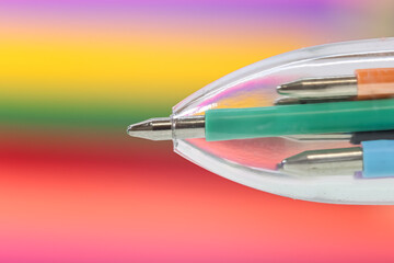 Close up view of multi colored ball point pen against colorful background.