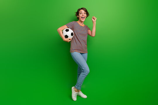 Full size photo of delighted pretty girl hand hold football raise fist success luck isolated on green color background