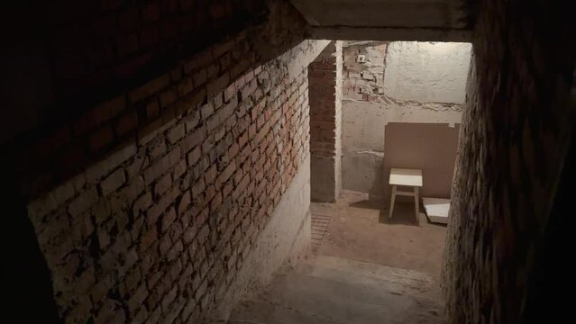 Entrance to an old dark underground basement or storeroom in an old house. Go down the stairs into the gloomy basement, where there is a chair against the brick wall. A basement bomb shelter