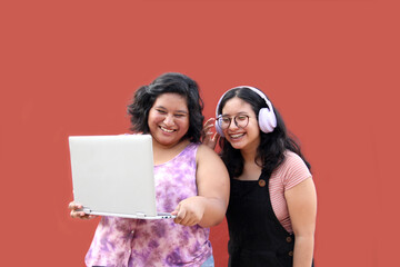 Two young 20 year old Latina brunette women use laptop and headphones for studying and entertainment watching music videos