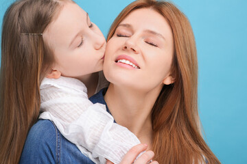 Portrait of happy mother and her cute daughter on light blue background, closeup