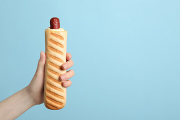Woman holding delicious french hot dog on light blue background, closeup. Space for text