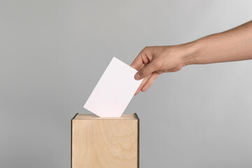 Man putting his vote into ballot box on light grey background, closeup