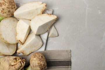 Whole and cut celery roots on grey marble table, flat lay. Space for text