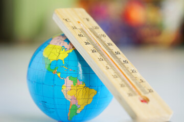 Wooden eco-friendly thermometer and globe on the background of a room or classroom interior. Temperature in Celsius and Fahrenheit. Climate change and global warming. Photo. Selective focus. Close-up