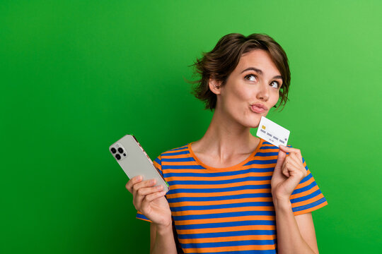 Photo portrait of attractive young woman look empty space gadget credit card wear trendy striped clothes isolated on green color background