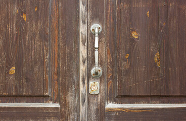 Fototapeta na wymiar Old wooden entrance door with a metal handle. A dilapidated, antique door with an iron handle.