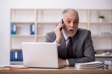 Old male employee speaking by phone at workplace