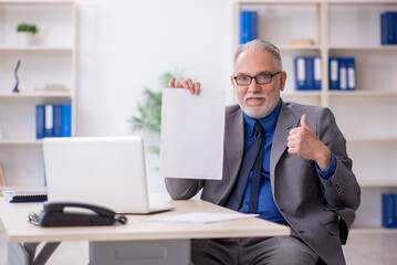Old male employee reading paper at workplace