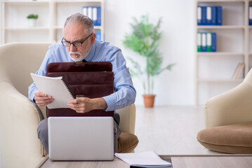 Old male employee sitting on arm-chair