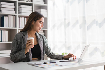 Businesswoman drinking coffee while checking finance document and typing business data on laptop