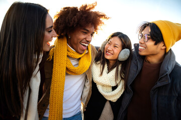 Multiethnic college student friends enjoying sunny winter day together. Young happy people embracing having fun outdoors - obrazy, fototapety, plakaty