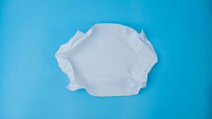 A paper ball is spread out into a blank sheet on blue background. Crumpled blank white paper with copy space for text or advertising space.