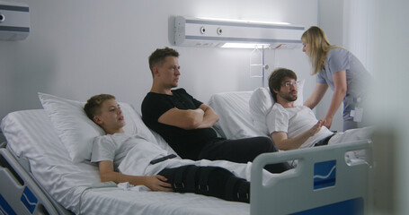 Father, kid and neighbor patient rest in hospital ward and emotionally watching sports championship. Nurse cares about patients. Modern bright medical center.