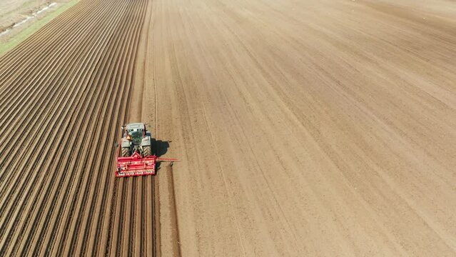 aerial view tractor cuts furrows in farm field for sowing farm tractor with rotary harrow plow preparing land for sowing. Tractor with harrows prepares the agricultural land for planting crop