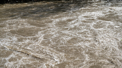 The river swollen after heavy rainfall and flood water crashing through valley. The water flows fast from the high valley to the plain. General contest of a river in flood