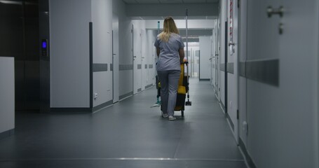 Adult nurse pushes cleaning trolley down medical center hallway. Health worker goes to hospital...