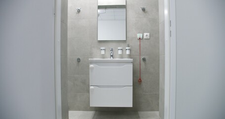 Dolly shot of white sink with mirror above it in bright and well-equipped bathroom with modern design in comfortable hospital ward. Sink, toilet and shower in medical facility or clinic. Zoom in.