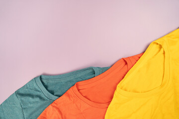 close up of rolled colorful t shirt clothes on pink table background, travel and lifestyle concept