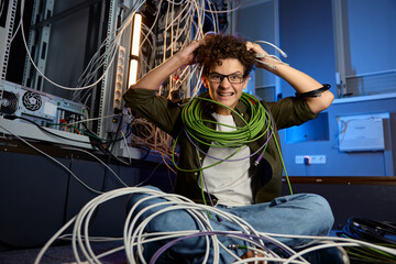 Stressed teenager geek wrapped in wire sitting on floor in data center