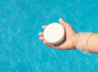 Human hand in protective glove holding white pill on background of blue clear water of swimming...