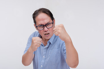 A middle aged asian man threatens to hit someone with his fist if they come closer. A hotheaded dad putting his guard stance up. Isolated on a white backdrop. - obrazy, fototapety, plakaty