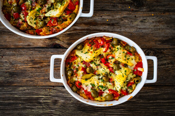 Bread casserole with mozzarella cheese, tomatoes, green olives, artichokes and scrambled eggs on wooden table
